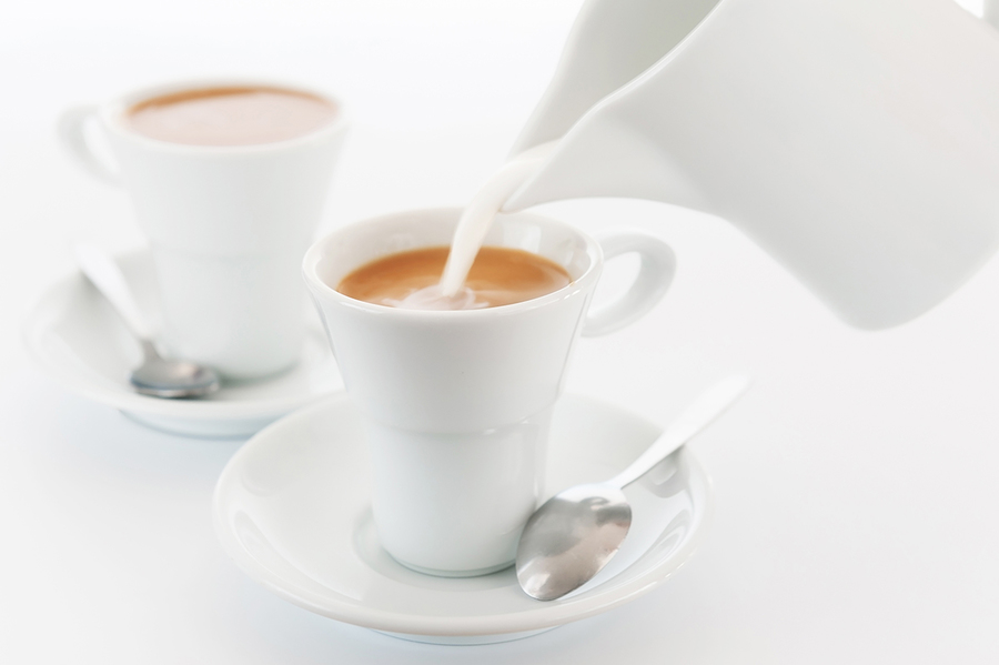 Milk is poured into a cup of coffee. White cups and a milkman on a white background. A large plan. An elective focus.