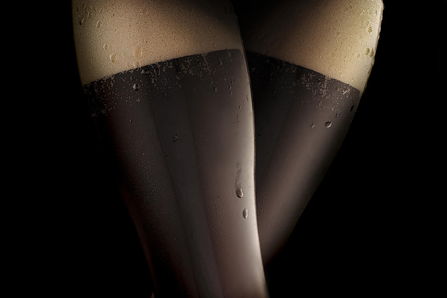 Dark cold beer in two steamed glasses, resembling sexy female legs in black stockings. Black background